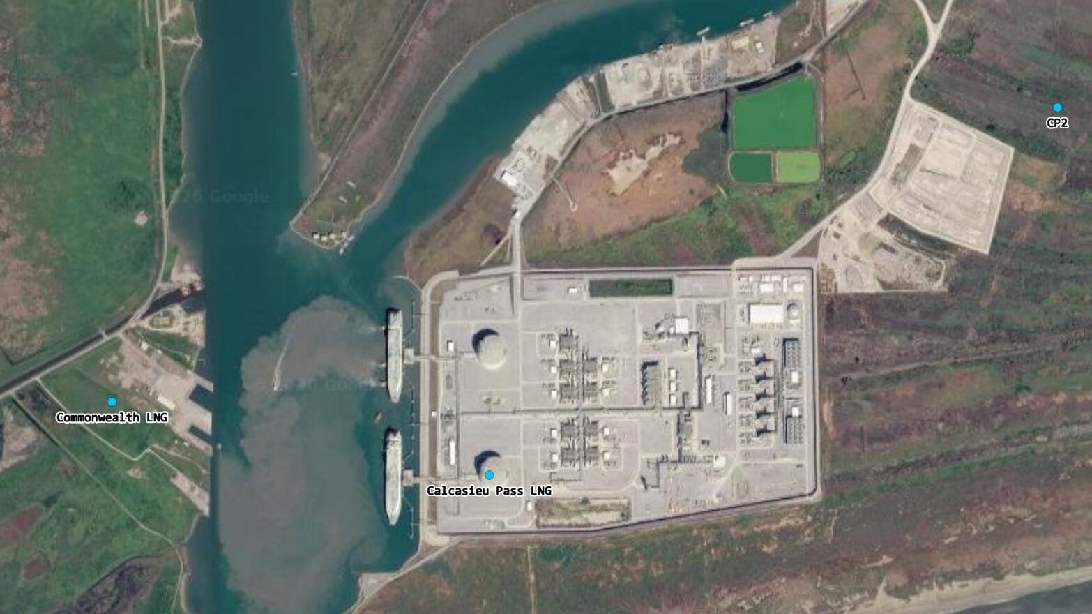 Aerial view of a coastal liquefied natural gas facility with docks, storage tanks, and industrial buildings along a channel, surrounded by marshland and access roads.