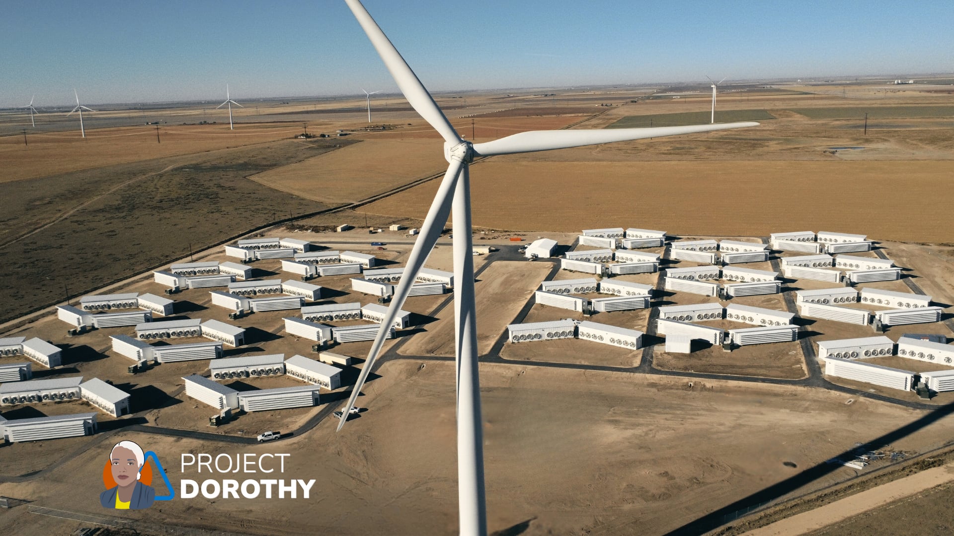 A windmill turns with the Project Dorothy data center campus in the background.