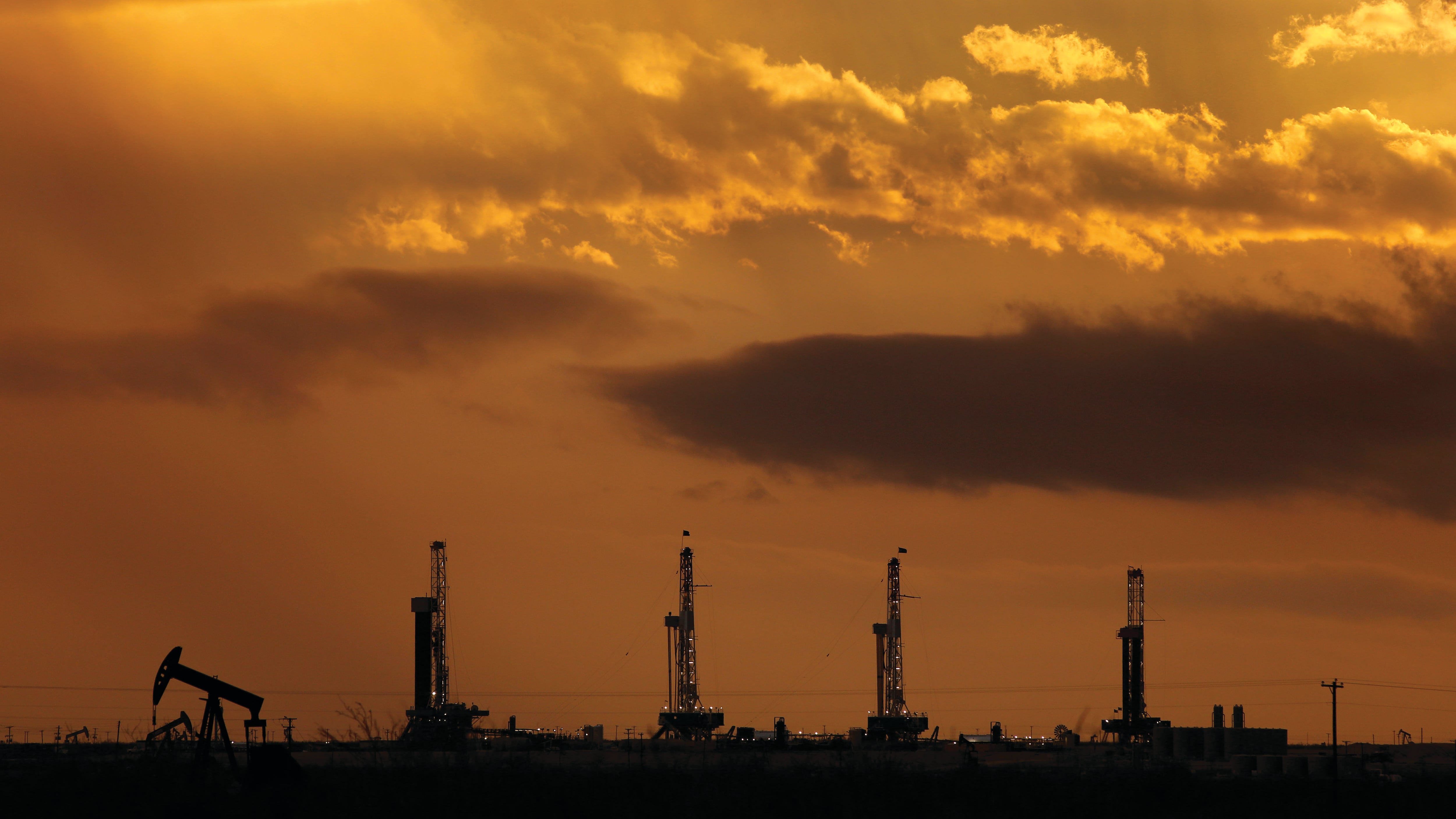 four fracking wells and one pumpjack silhouetted against a sunset sky