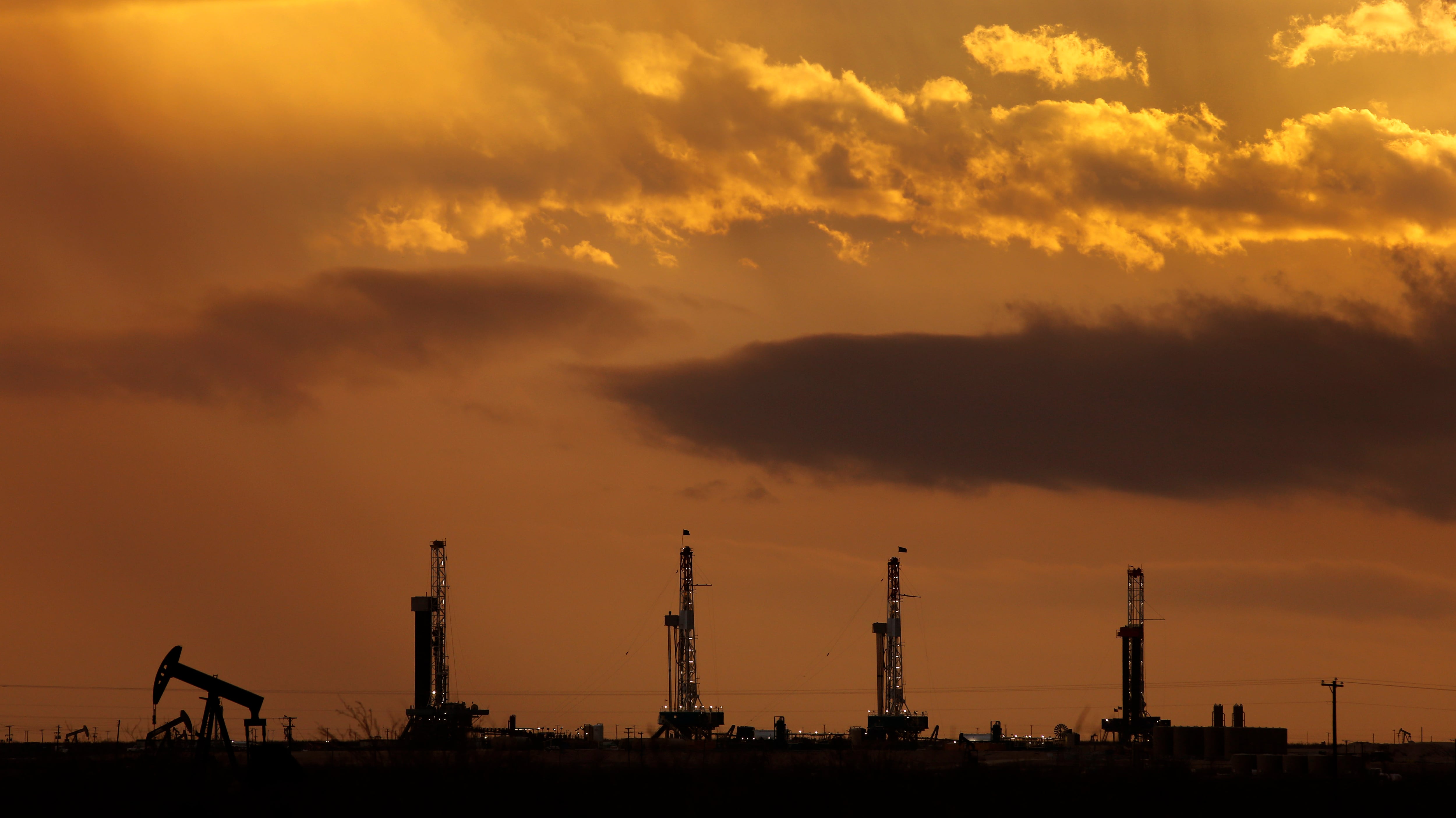 The sun sets on the west Texas horizon as a thunderstorm approaches four drilling rigs lined up on Pioneer Resources well sites south of Midland, Texas, Monday, February 22, 2016.